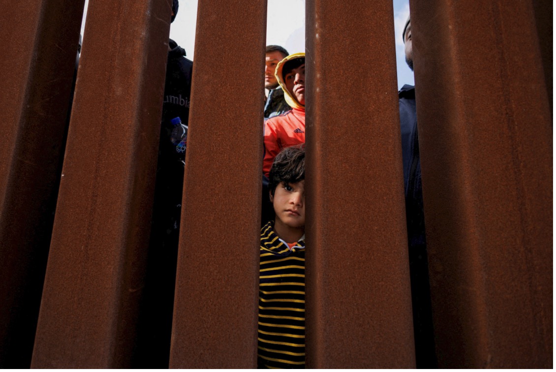 A young boy peers through the border wall as migrants gather between primary and secondary border fences in San Diego as the United States prepares to lift COVID-19-era restrictions known as Title 42, that have blocked migrants at the U.S.- Mexico border from seeking asylum since 2020, near San Diego on May 8, 2023. Photo by Mike Blake, Reuters